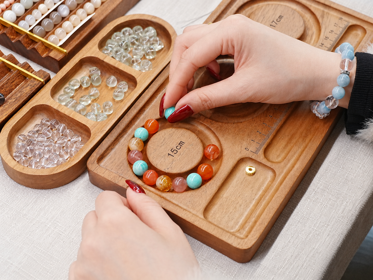 Hands arranging beads on a wooden design tray